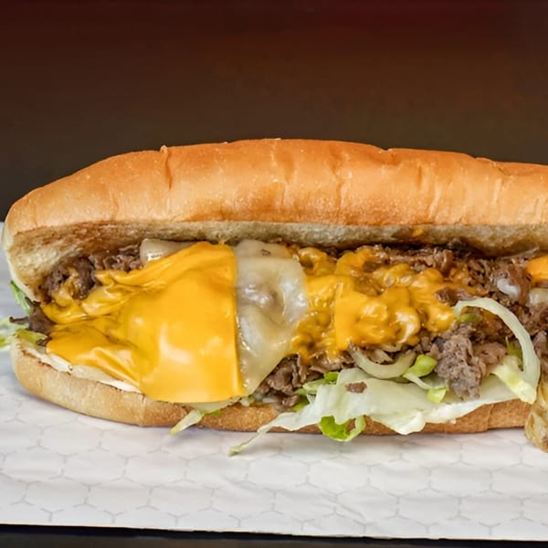 A Two Brothers Chicken cheesesteak sandwich with melted yellow and white cheese, steak, onions, and lettuce.