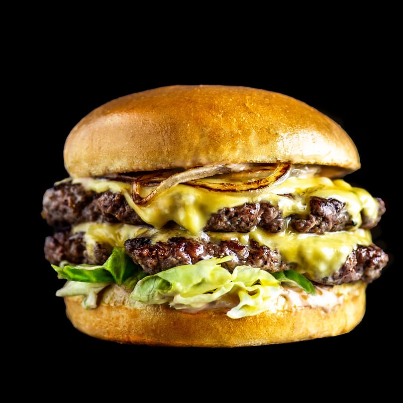 A double cheeseburger with melted cheese, caramelized onions, lettuce, and sauce on a brioche bun.