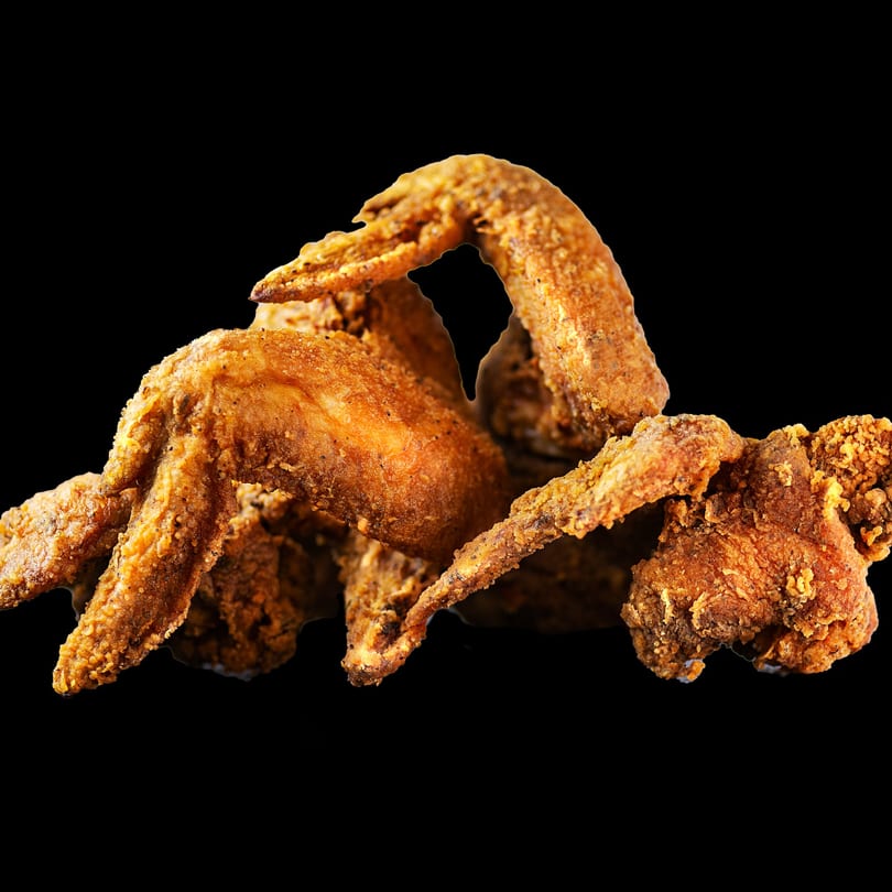 A pile of crispy, golden-brown fried chicken wings from Two Brothers Chicken on a black background.