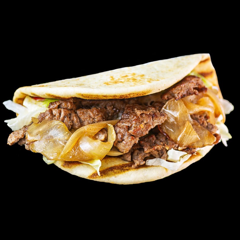 A beef shawarma wrap with grilled onions and lettuce, served on a flatbread.