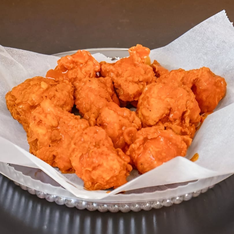 A platter of Two Brothers Chicken's crispy, orange-glazed fried chicken pieces on white parchment paper.
